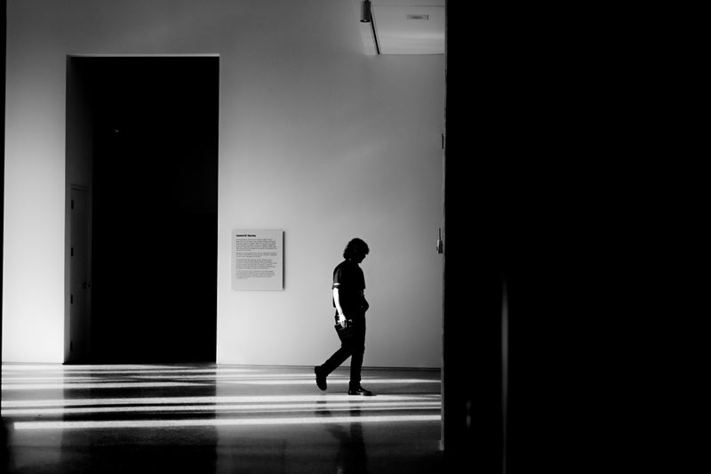 Black and white photo of a person silhouetted walking in a modern, minimalist indoor space.