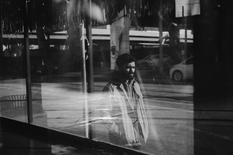 Black and white reflection of a man through a glass window in an urban street scene.