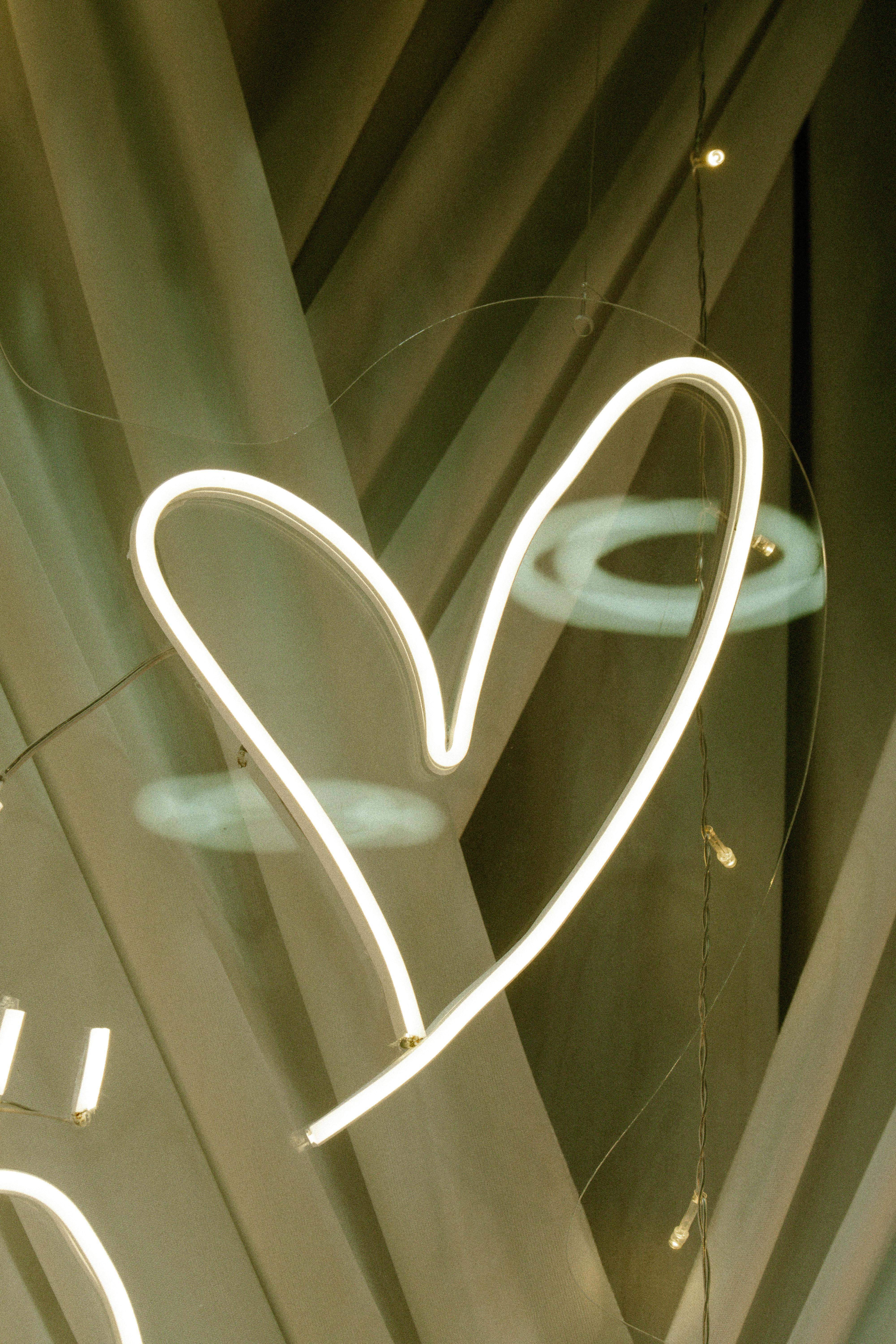 Free A glowing heart-shaped neon light art installation against geometric abstract background. Stock Photo