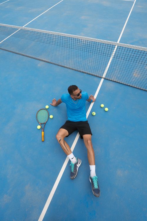 Free A man in sportswear relaxing on a blue tennis court with scattered tennis balls. Stock Photo