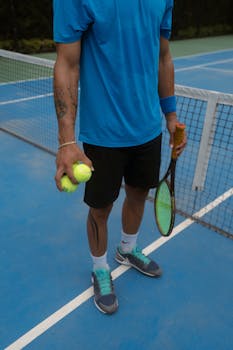Athlete holding tennis balls and racket on a blue outdoor court, ready for a match.