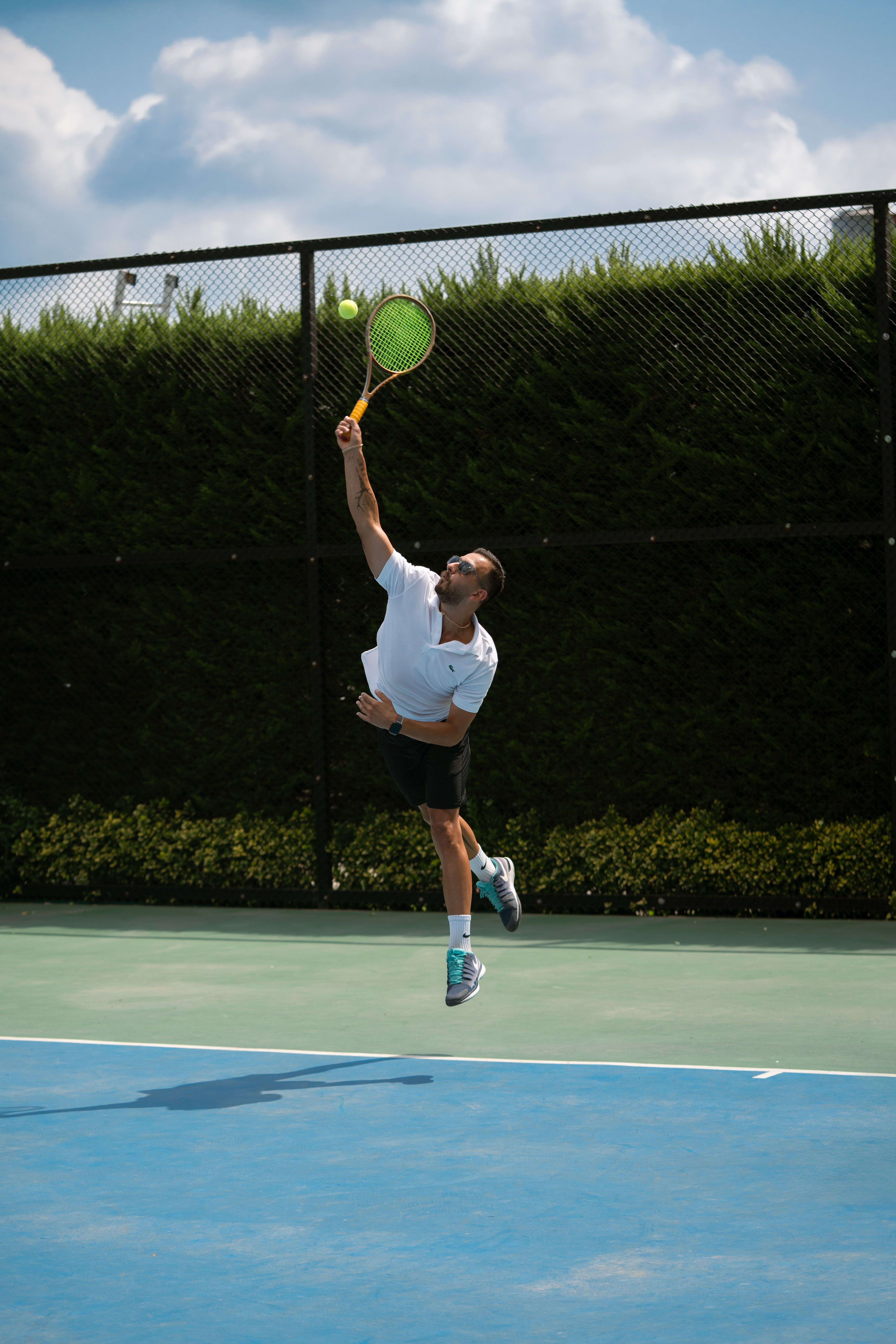 Athlete performs a powerful tennis serve on an outdoor court in Iran.