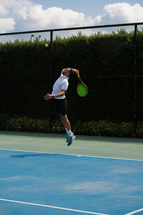 Free Athlete executing a powerful tennis serve under a clear sky on an outdoor court. Stock Photo