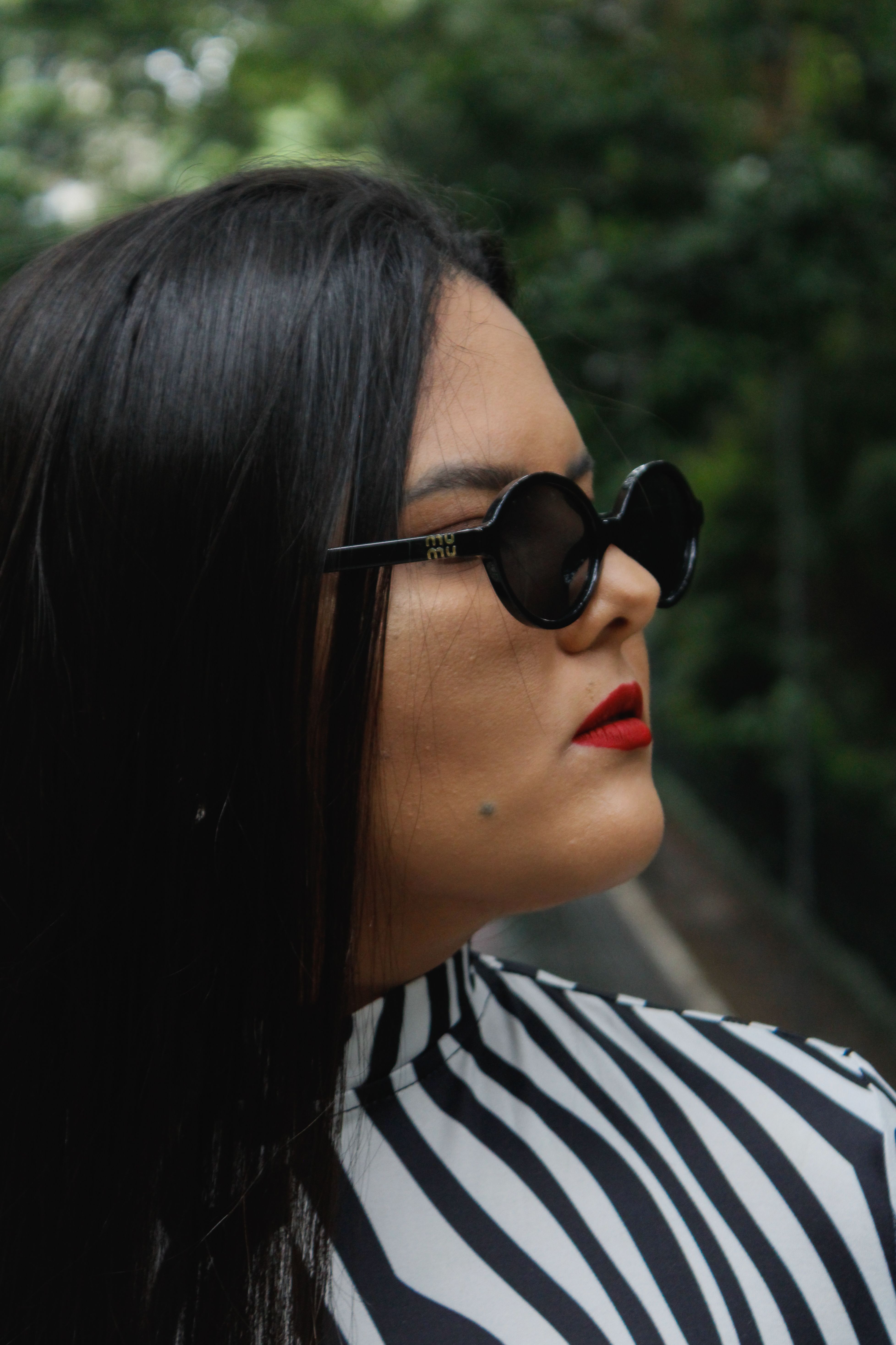 Profile of a woman wearing sunglasses and zebra print top in a natural setting.