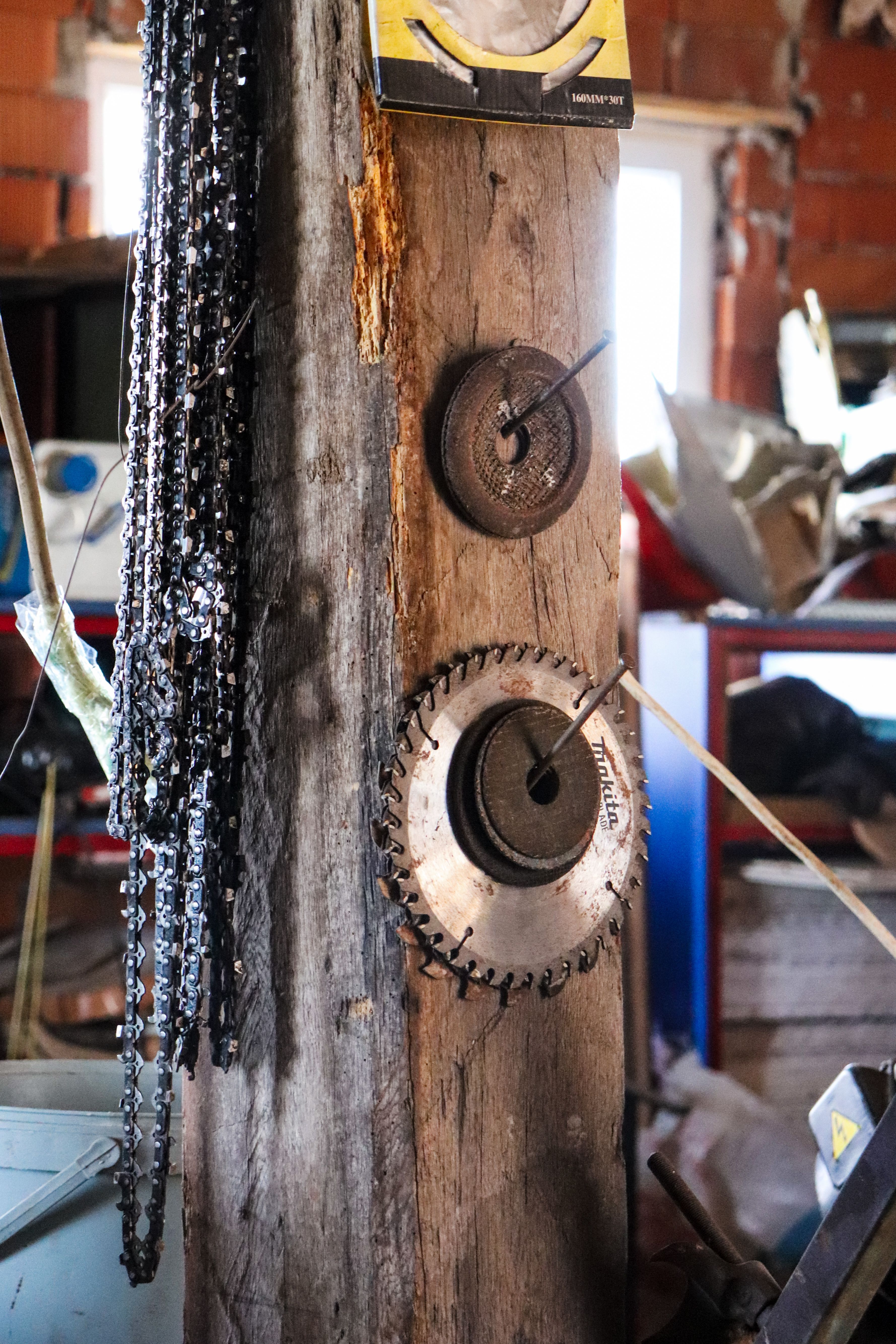 Interior of a rustic workshop featuring various saw blades and chains hanging on a wooden beam.