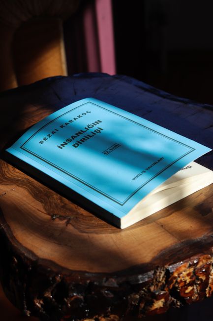 A blue book titled 'İnsanlığın Dirilişi' on a wooden table, bathed in warm light.