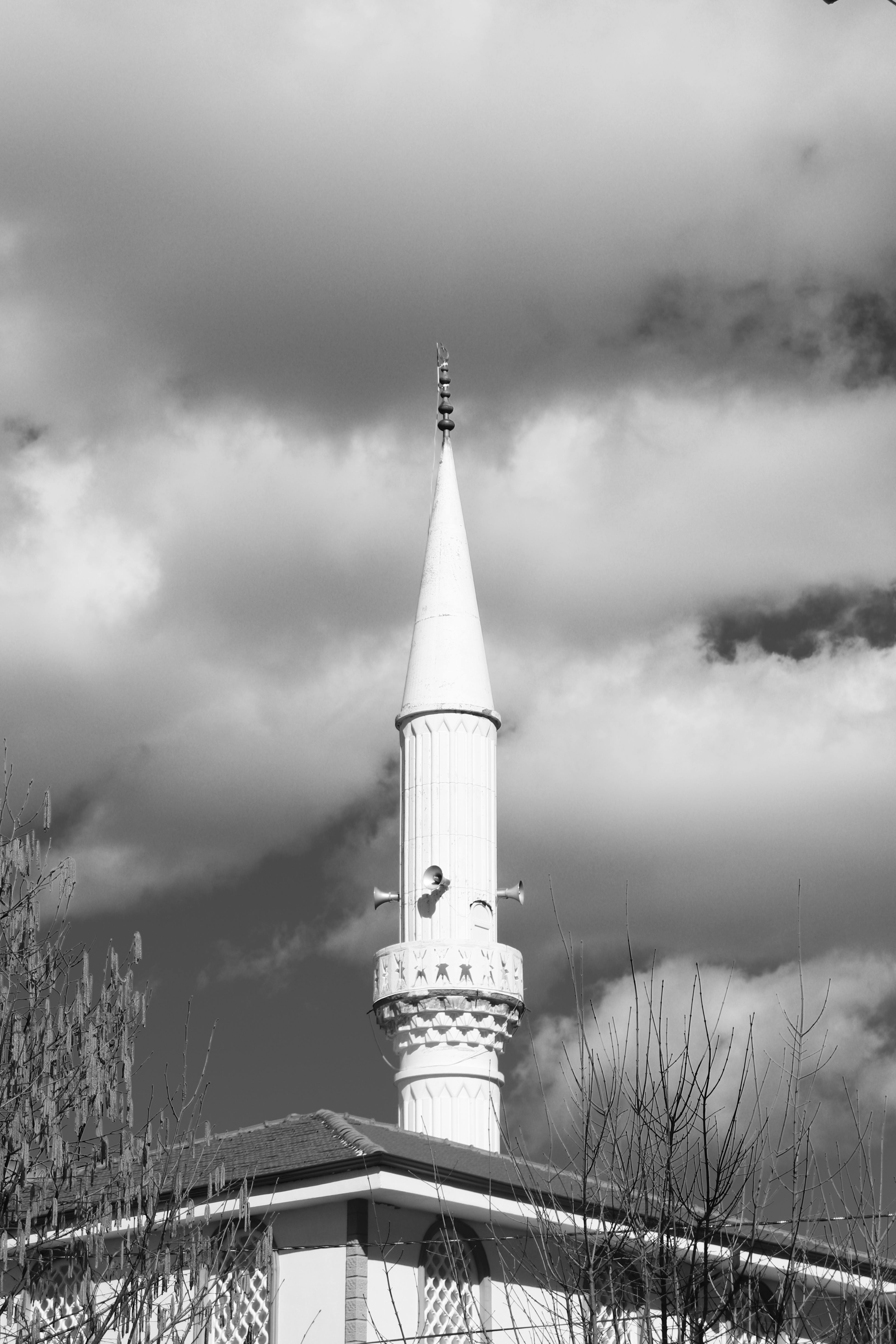 Kostenlos Schwarz-Weiß-Fotografie eines Moscheeminaretts vor einem dramatisch bewölkten Himmel. Stock-Foto