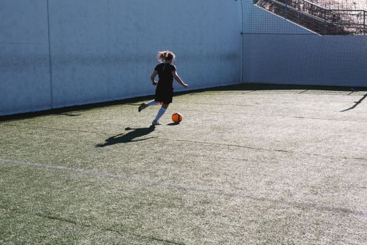 A young woman playing soccer, dribbling a ball on an outdoor field in daylight.