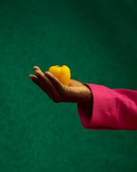 A vibrant yellow tomato cradled in a hand with a pink sleeve against a rich green backdrop.