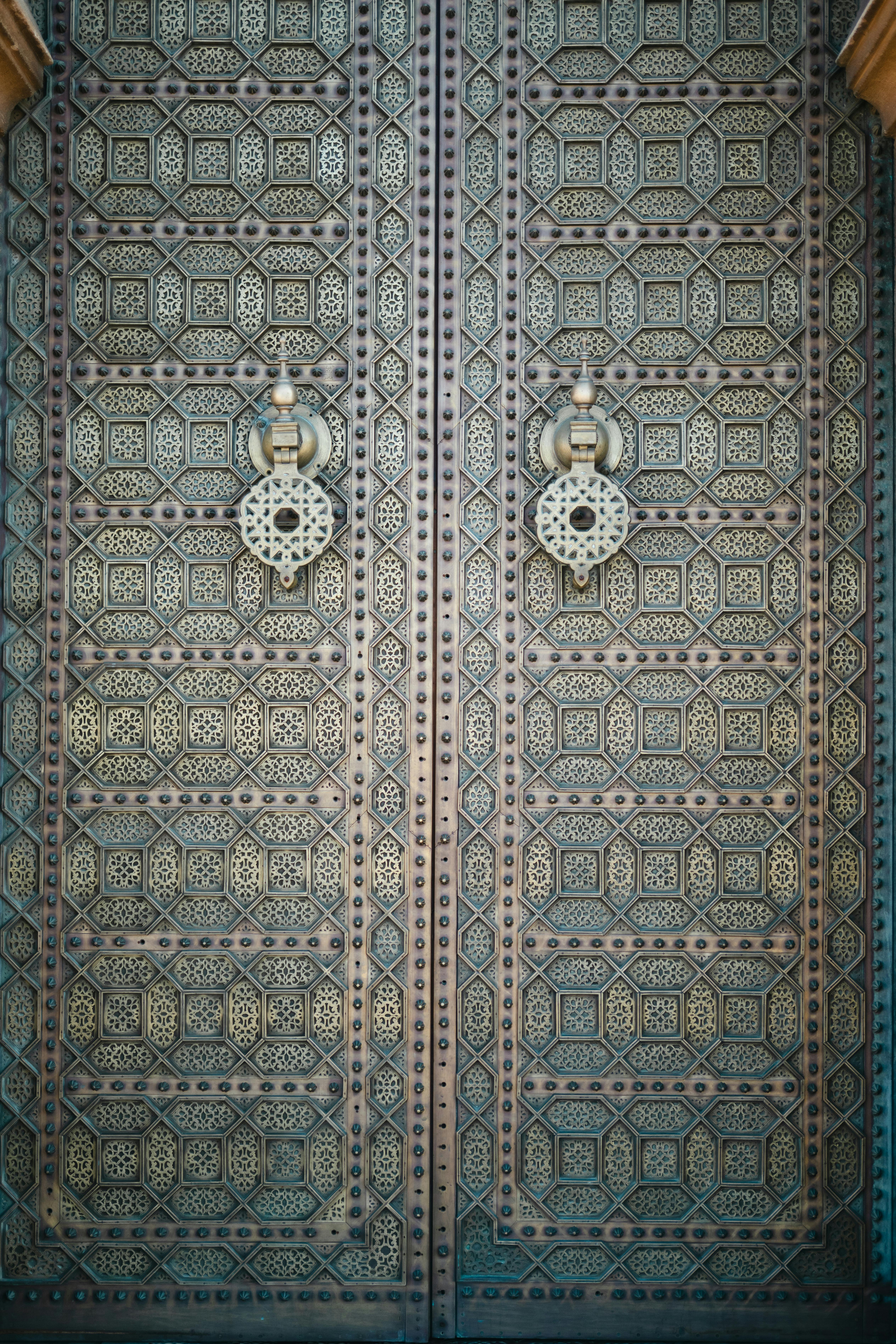 Gratis Primer plano de una puerta de metal adornada con detalles, patrones geométricos intrincados y dos manijas de aldaba. Foto de stock