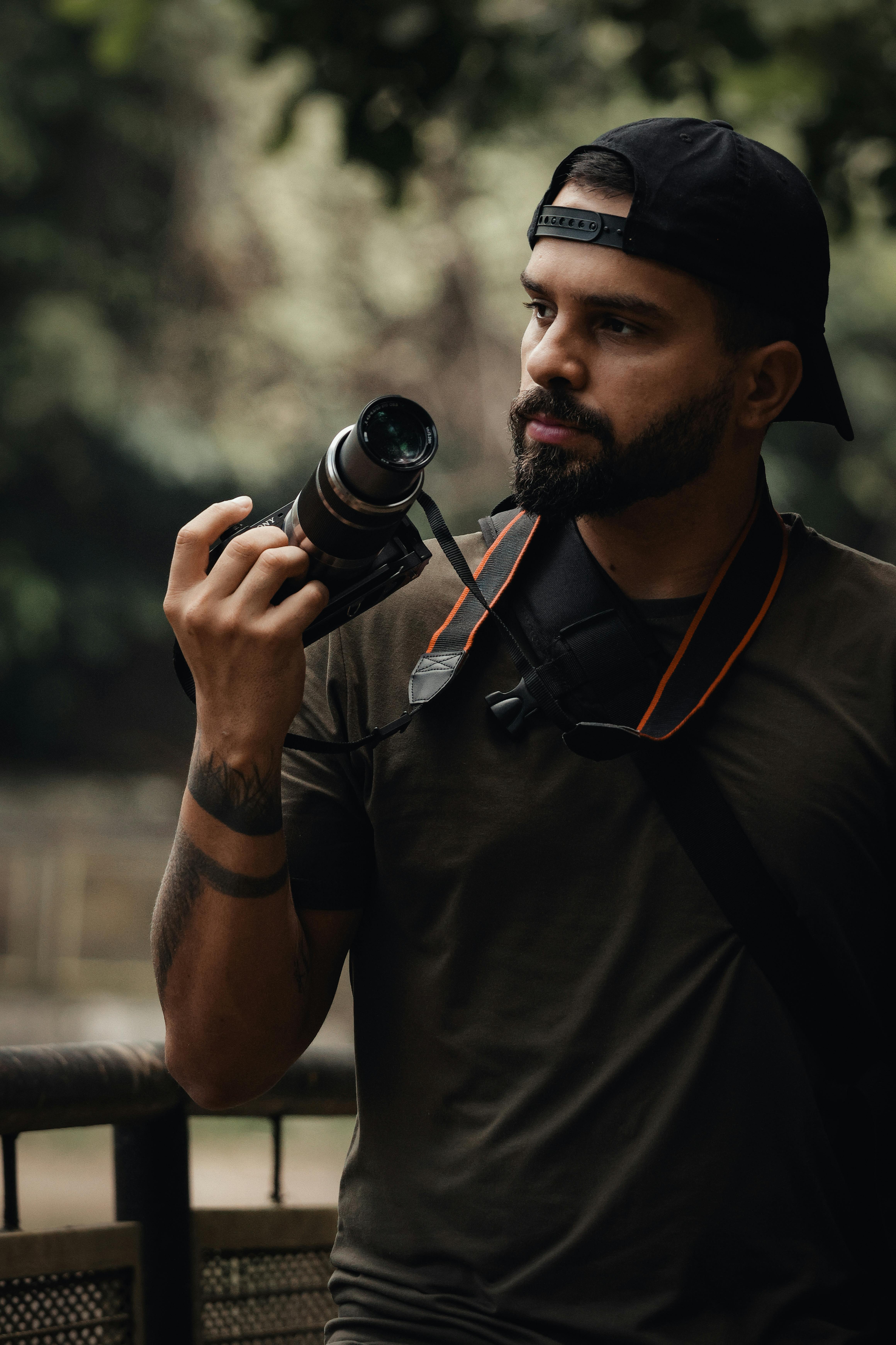 Ücretsiz Dış mekanda elinde kamerasıyla düşünceli bir halde duran, profesyonel bir hava yayan erkek fotoğrafçı. Stok Fotoğraflar