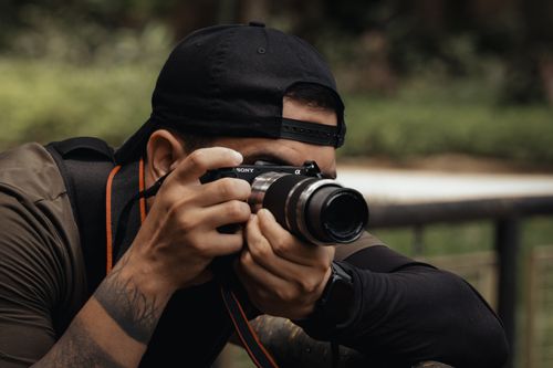 Free A man wearing a cap and taking photos outdoors with a DSLR camera, focused on capturing the moment. Stock Photo