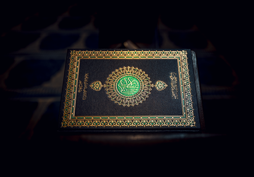 Free Islamic Holy Quran book with ornate gold detailing, resting on a patterned surface. Stock Photo