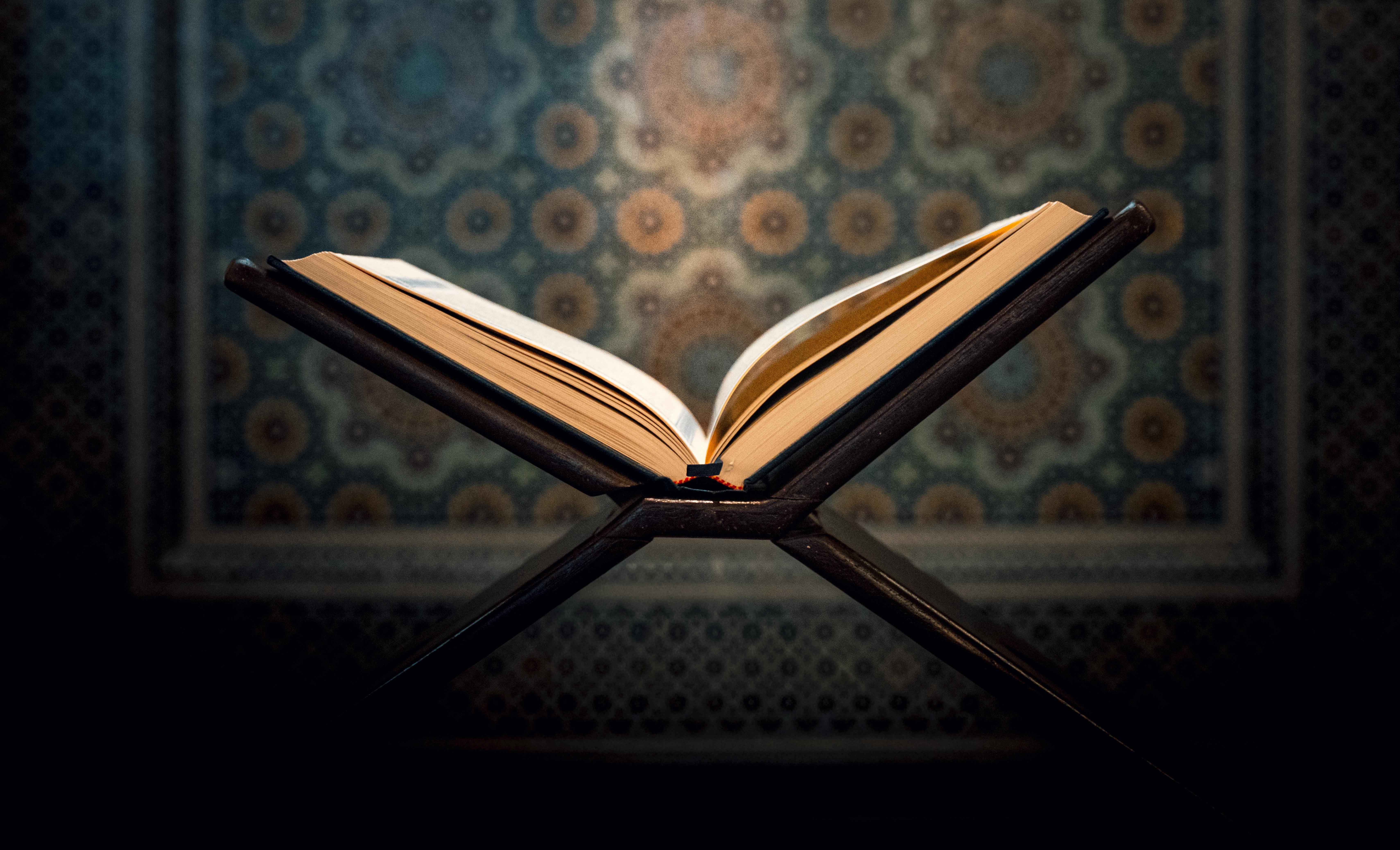 Gratuit O carte deschisă a Coranului pe un suport într-o moschee din Kuweit, cu un fundal de arhitectură islamică complexă. Fotografie de stoc