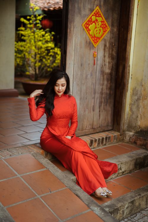 Free Elegant woman in traditional red dress sitting by a wooden door, showcasing cultural fashion. Stock Photo