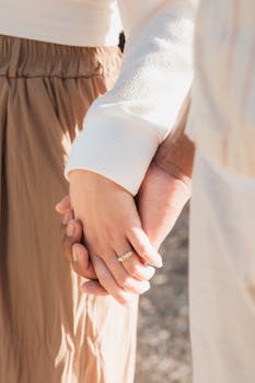 Close-up of a couple holding hands outdoors, featuring an engagement ring, symbolizing love and connection.