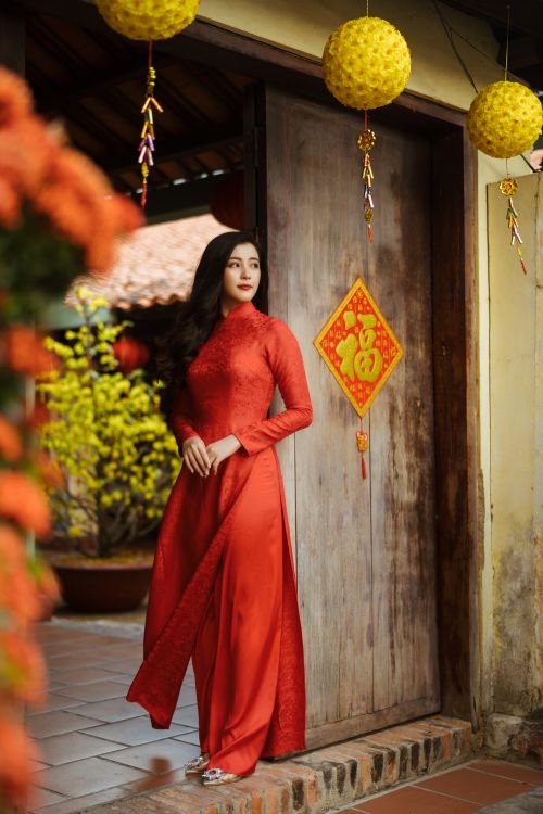 Free A woman in red traditional attire stands by a decorated wooden door for Lunar New Year. Stock Photo