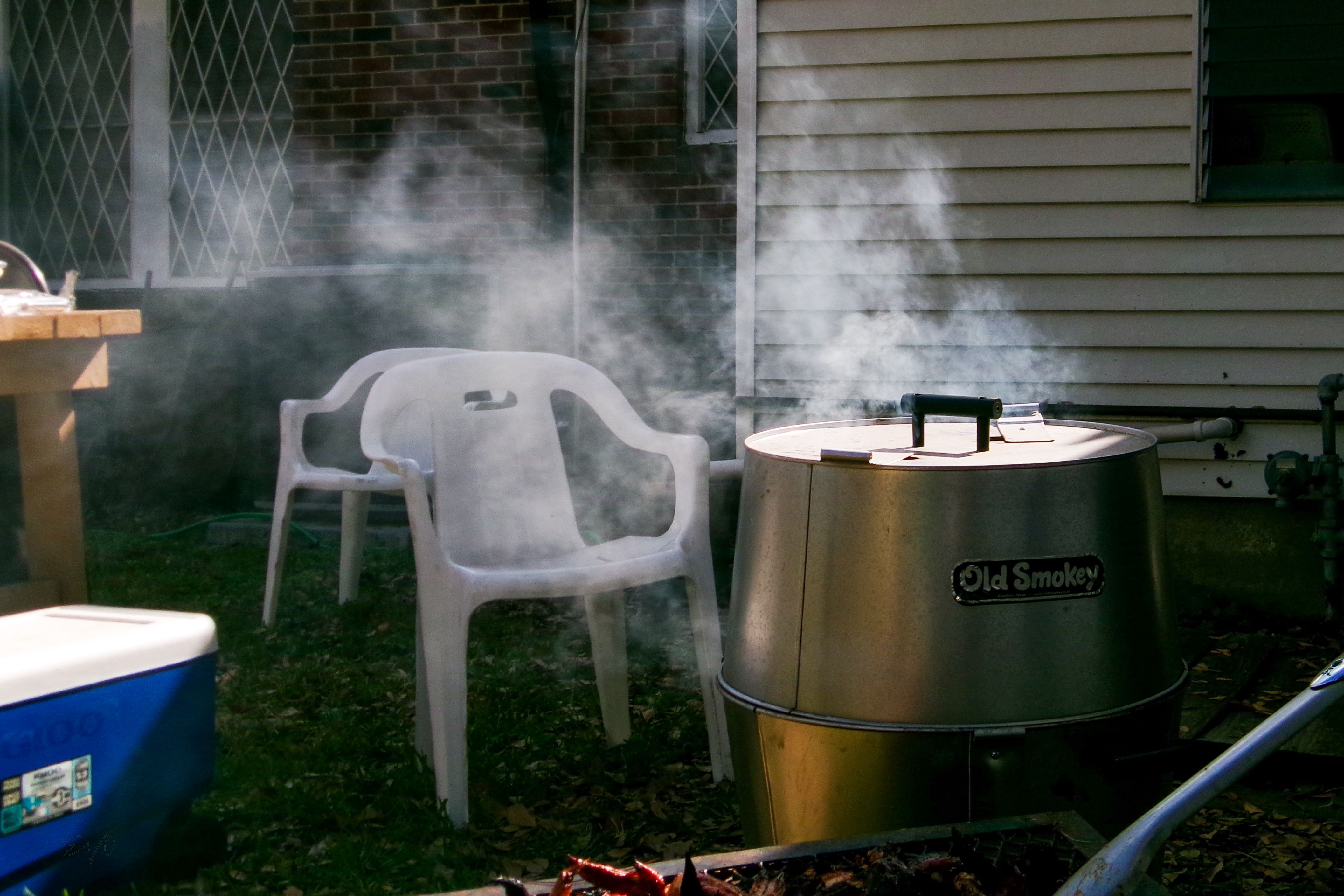 Smoke rising from a barbecue grill beside empty chairs in a Houston backyard setting.