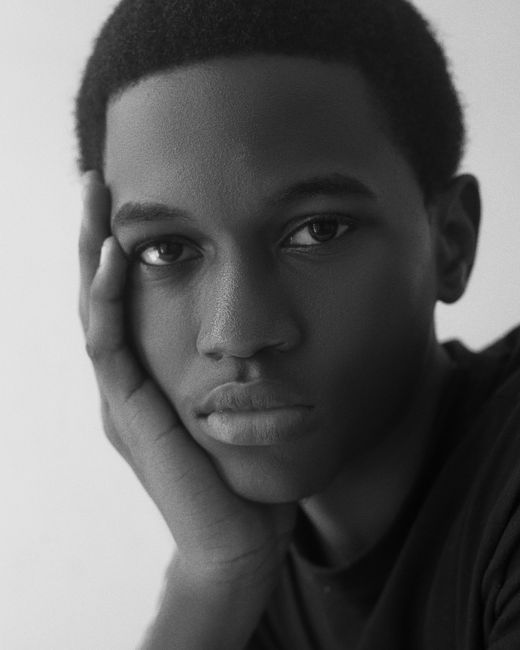 A thoughtful black and white portrait of a young African man resting his face on his hand, evoking contemplation.