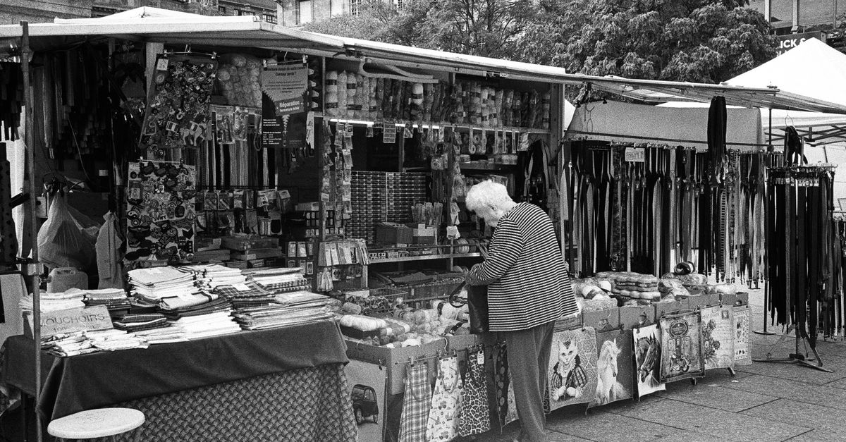 Black and white photo of an elderly woman exploring a bustling outdoor market in Strasbourg.
