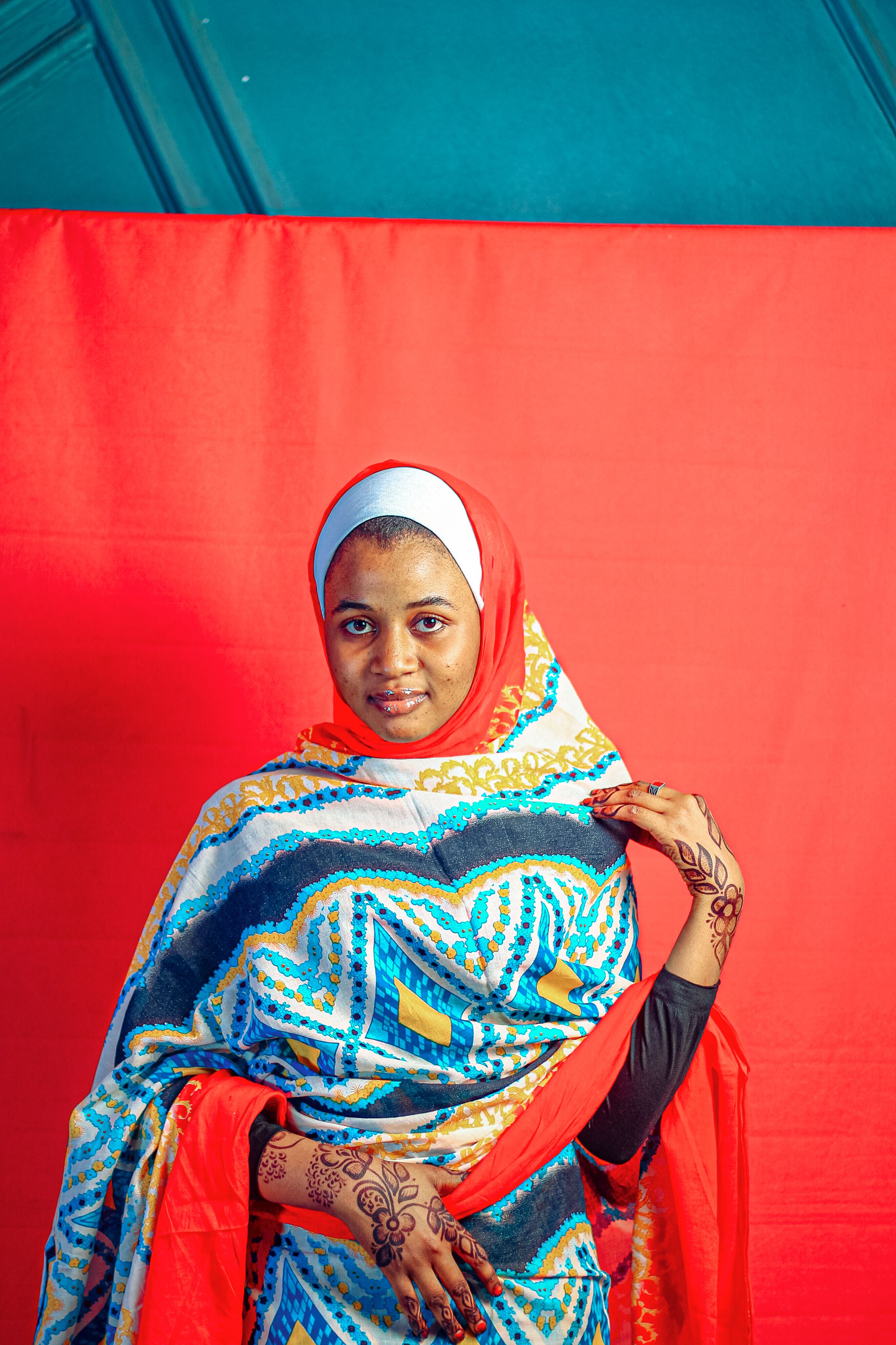 A vibrant portrait of a woman in traditional attire with henna, against a red backdrop.