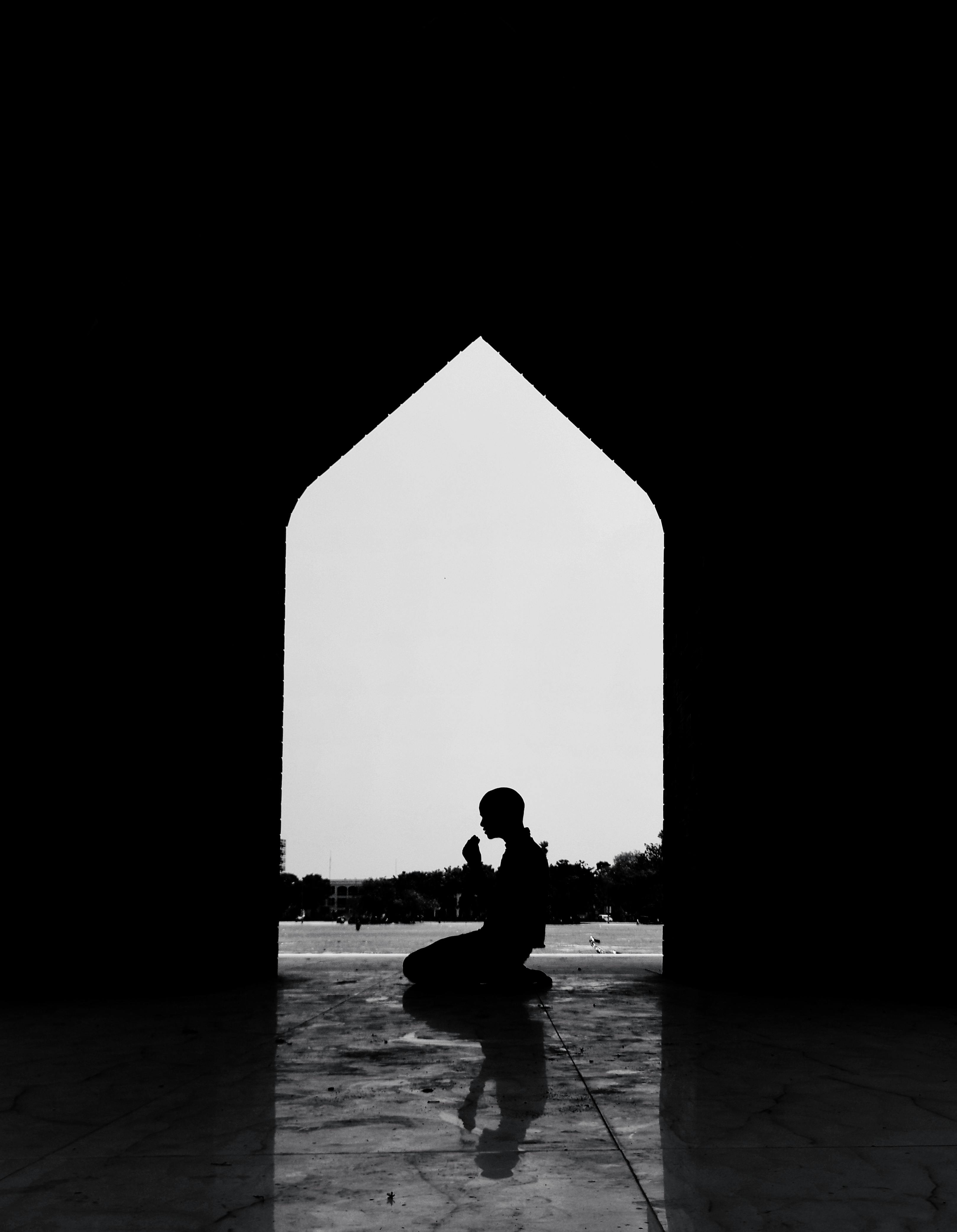 Bezpłatne Potężna sylwetka człowieka modlącego się na zewnątrz łuku, oddająca spokój i duchowość. Zdjęcie z galerii