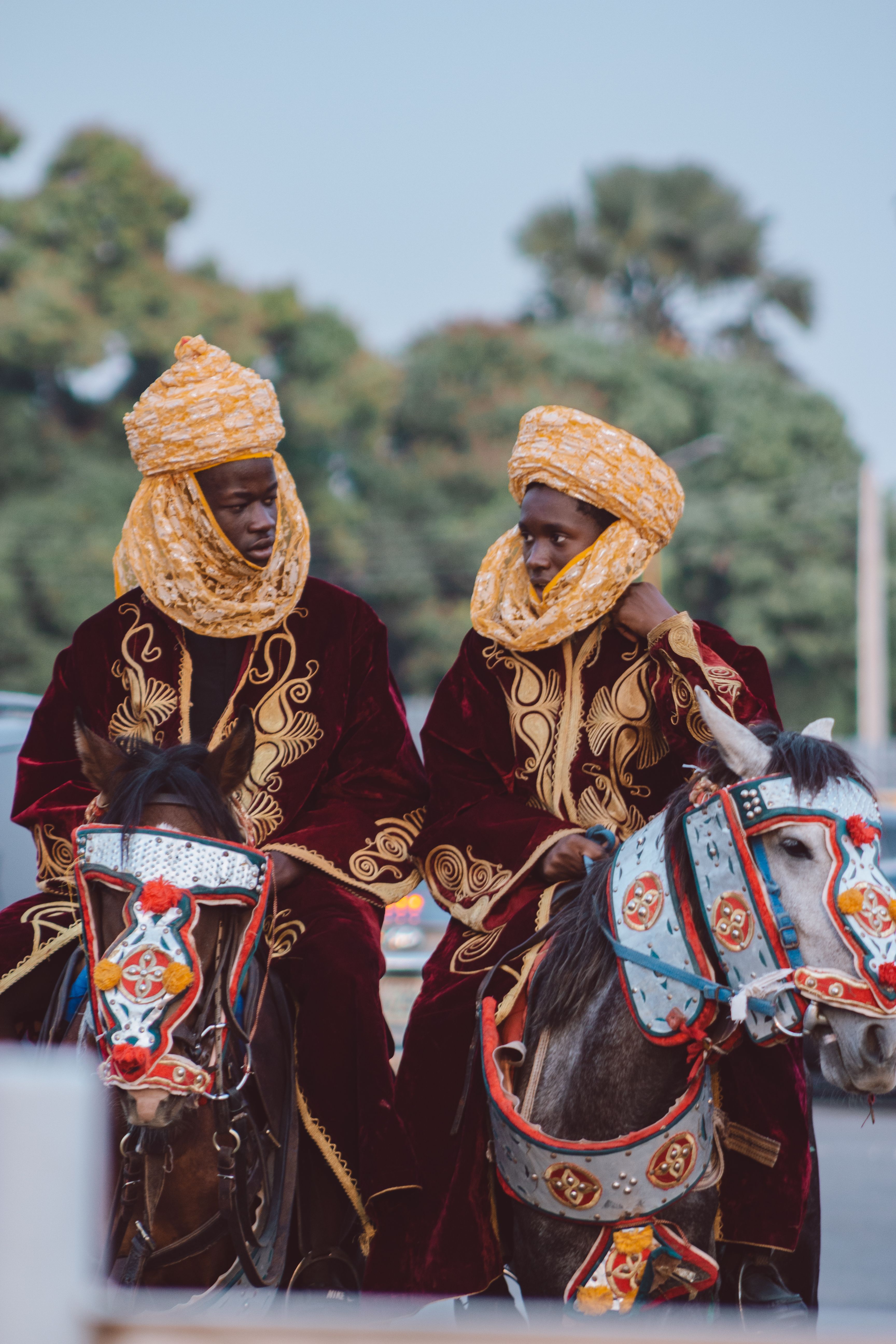 Two men in traditional attire riding decorated horses at a cultural event, showcasing heritage.