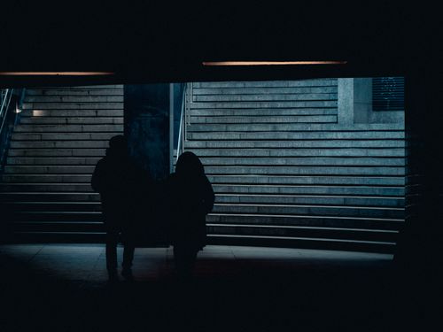 Free Silhouette of two people in a dimly lit urban underpass with stairs. Stock Photo