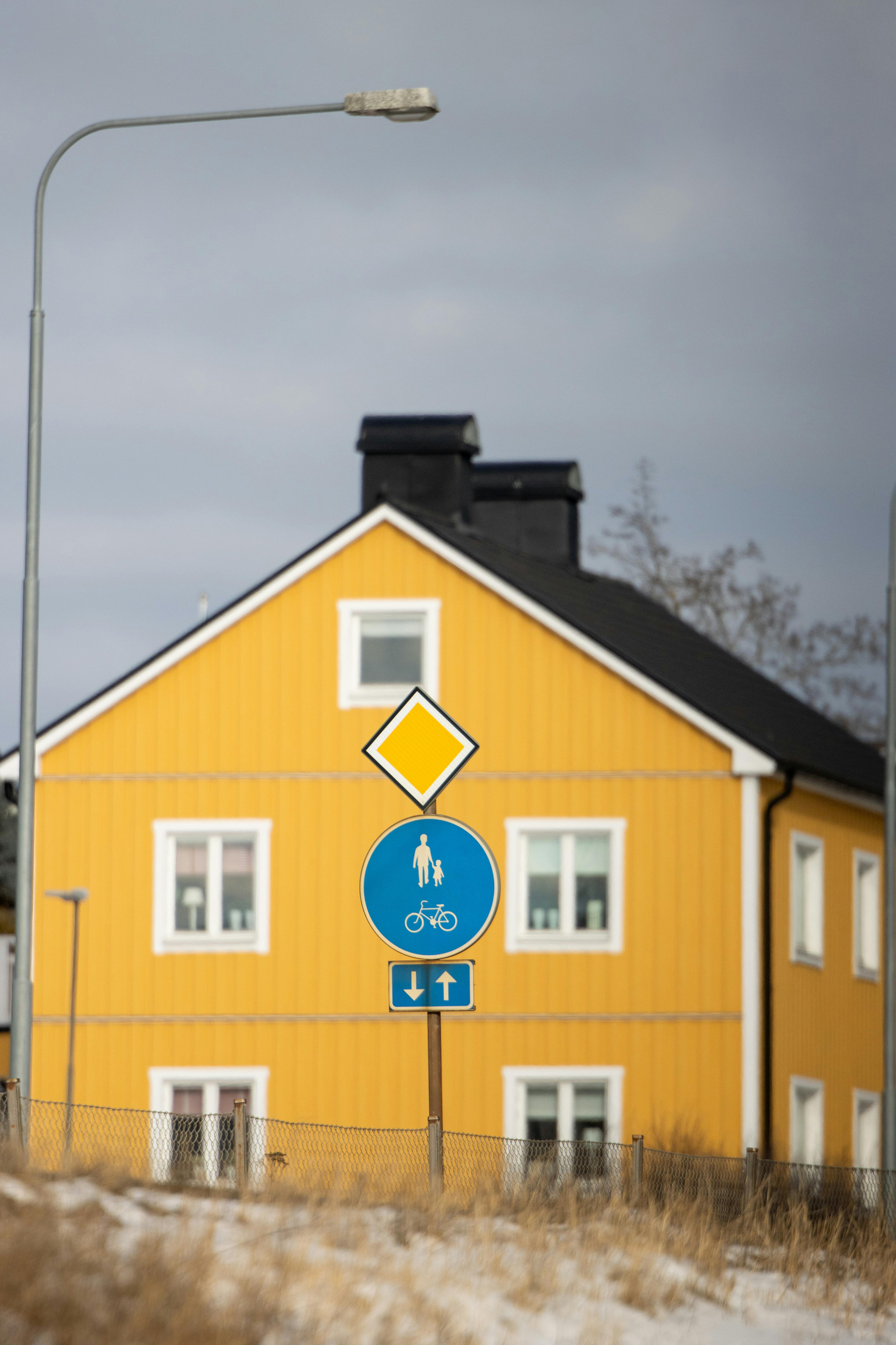 Δωρεάν Ένα φωτεινό κίτρινο σπίτι με πινακίδες πεζών και ποδηλάτων σε έναν συννεφιασμένο ουρανό στο Γιένσεπινγκ της Σουηδίας. Φωτογραφία από στοκ φωτογραφιών