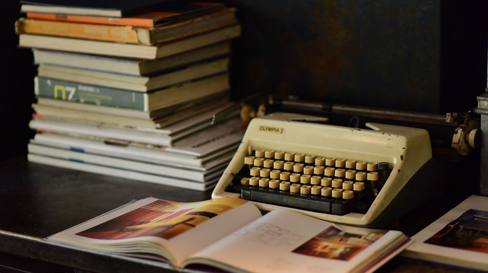 A nostalgic scene with an old typewriter and a stack of books on a wooden desk.