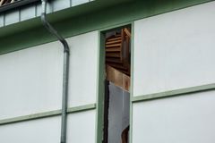 An exterior view of a damaged house showing a broken roof and exposed interior structure.