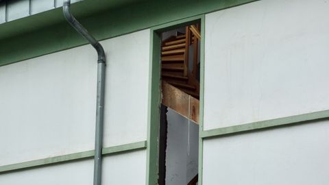 An exterior view of a damaged house showing a broken roof and exposed interior structure.