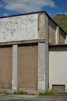 Exterior view of an old industrial building with visible wear, set against a partly cloudy sky.