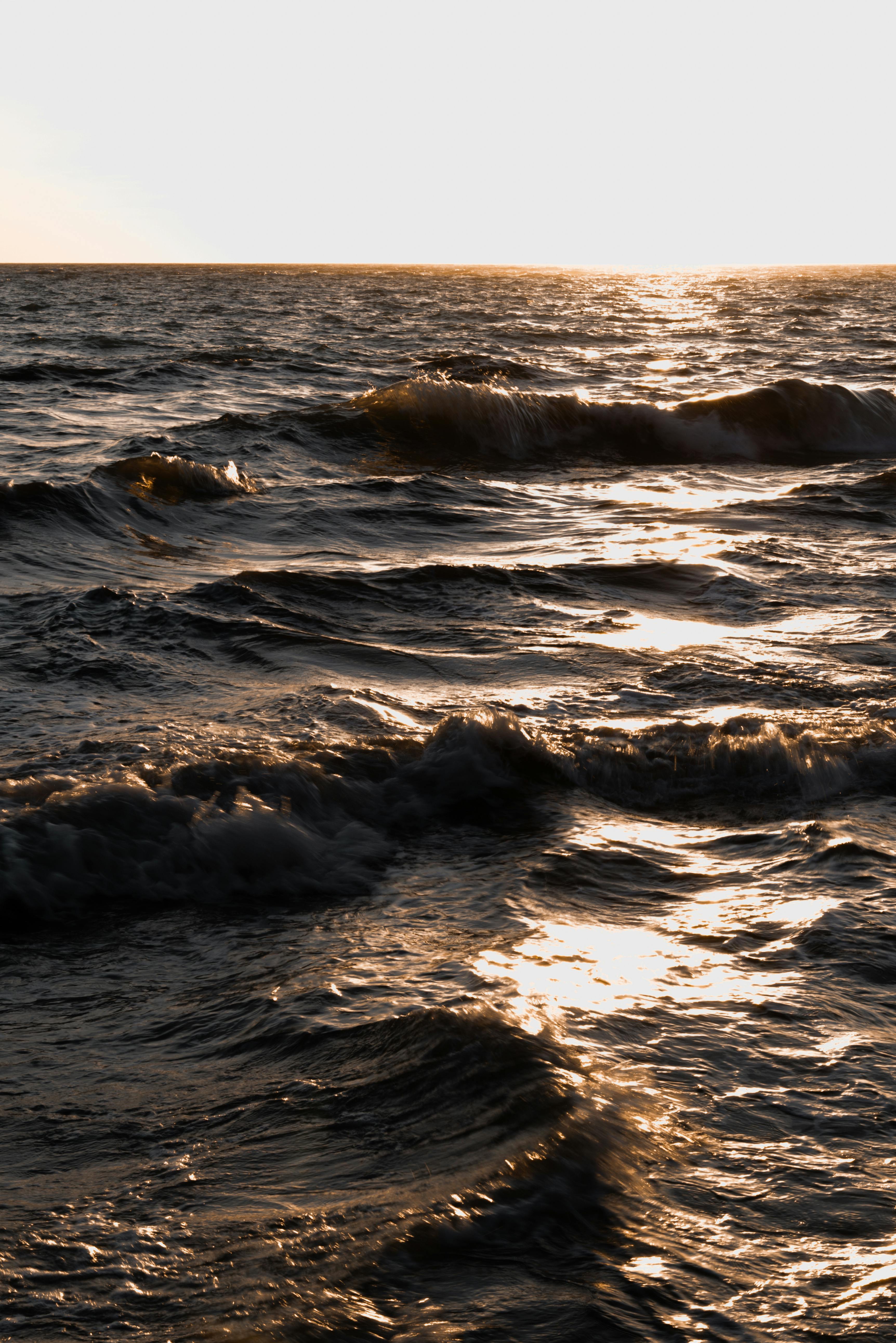 Gratis Gyllent sollys reflekterer på havbølger under solnedgang, og skaper et dramatisk sjølandskap. Arkivbilde