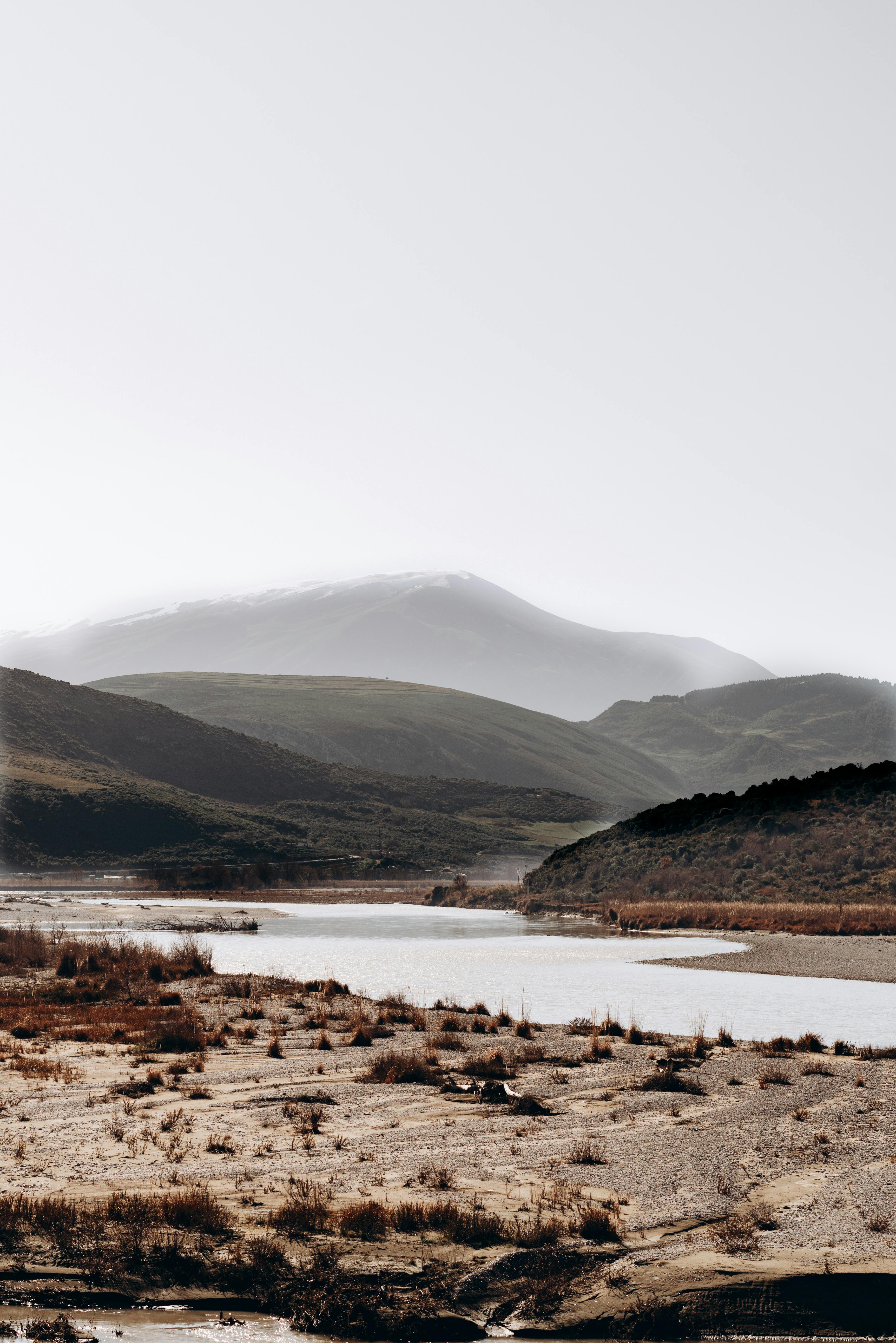 Δωρεάν Γαλήνιο ορεινό τοπίο με ένα ήρεμο ποτάμι και κυματιστούς λόφους κάτω από έναν λαμπερό ουρανό. Φωτογραφία από στοκ φωτογραφιών