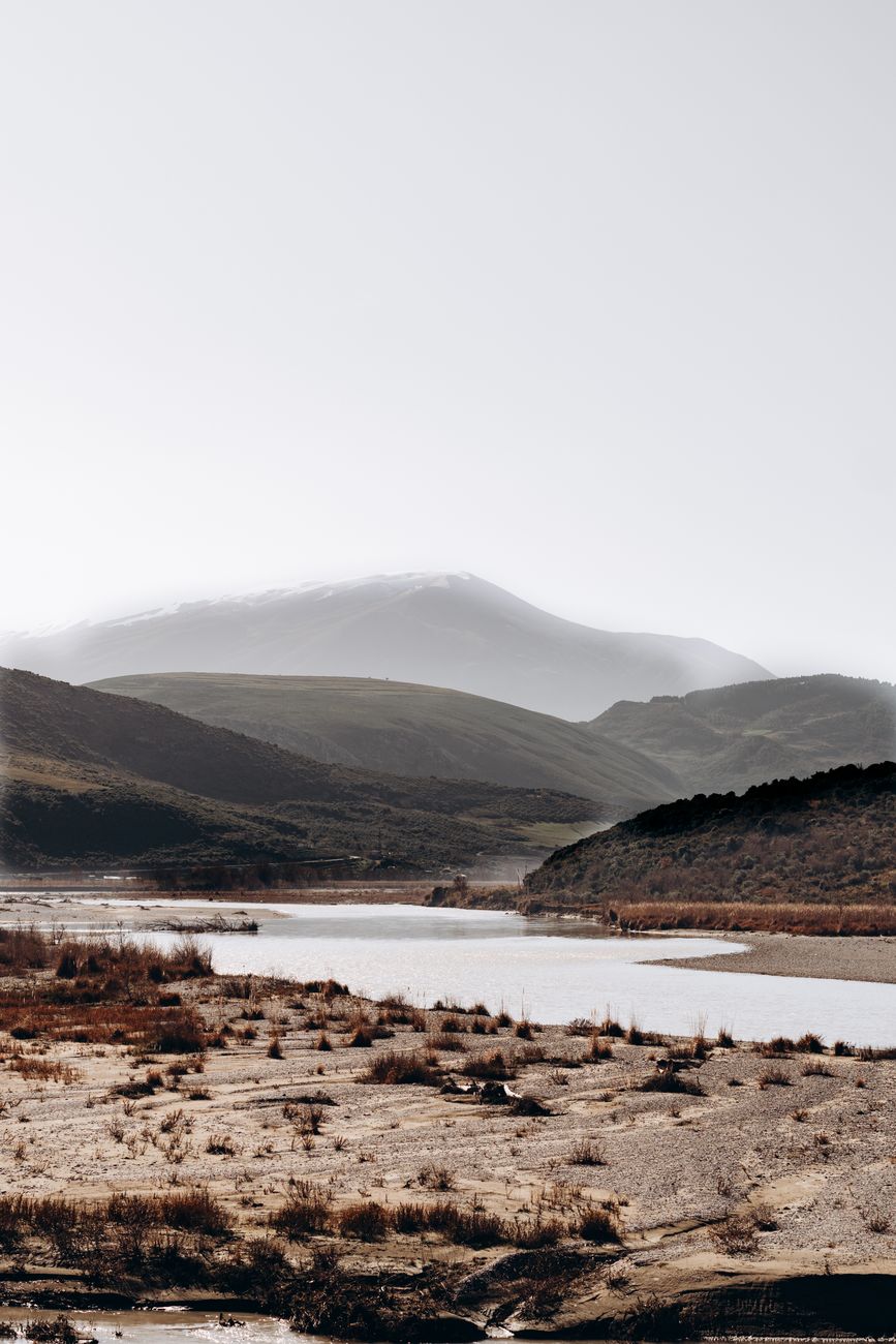 Serene mountain landscape featuring a calm river and rolling hills under a bright sky.