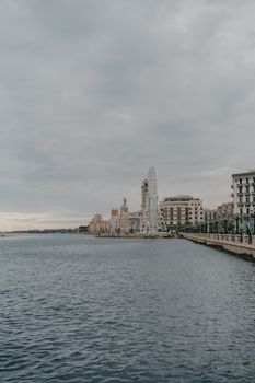 View of a coastal cityscape under an overcast sky, featuring a Ferris wheel along the waterfront.