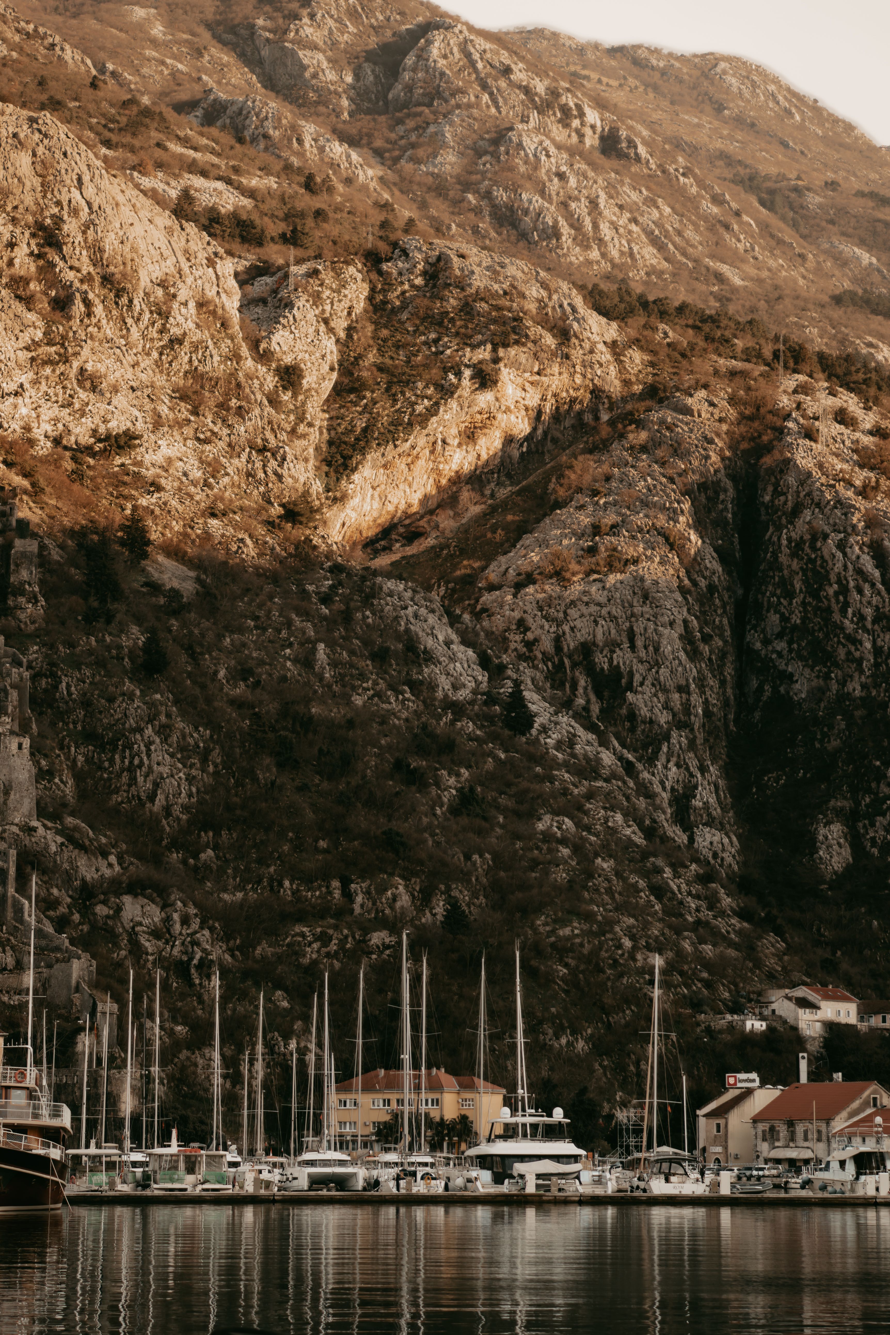 Scenic view of sailboats in a marina with a majestic mountain backdrop under soft daylight.