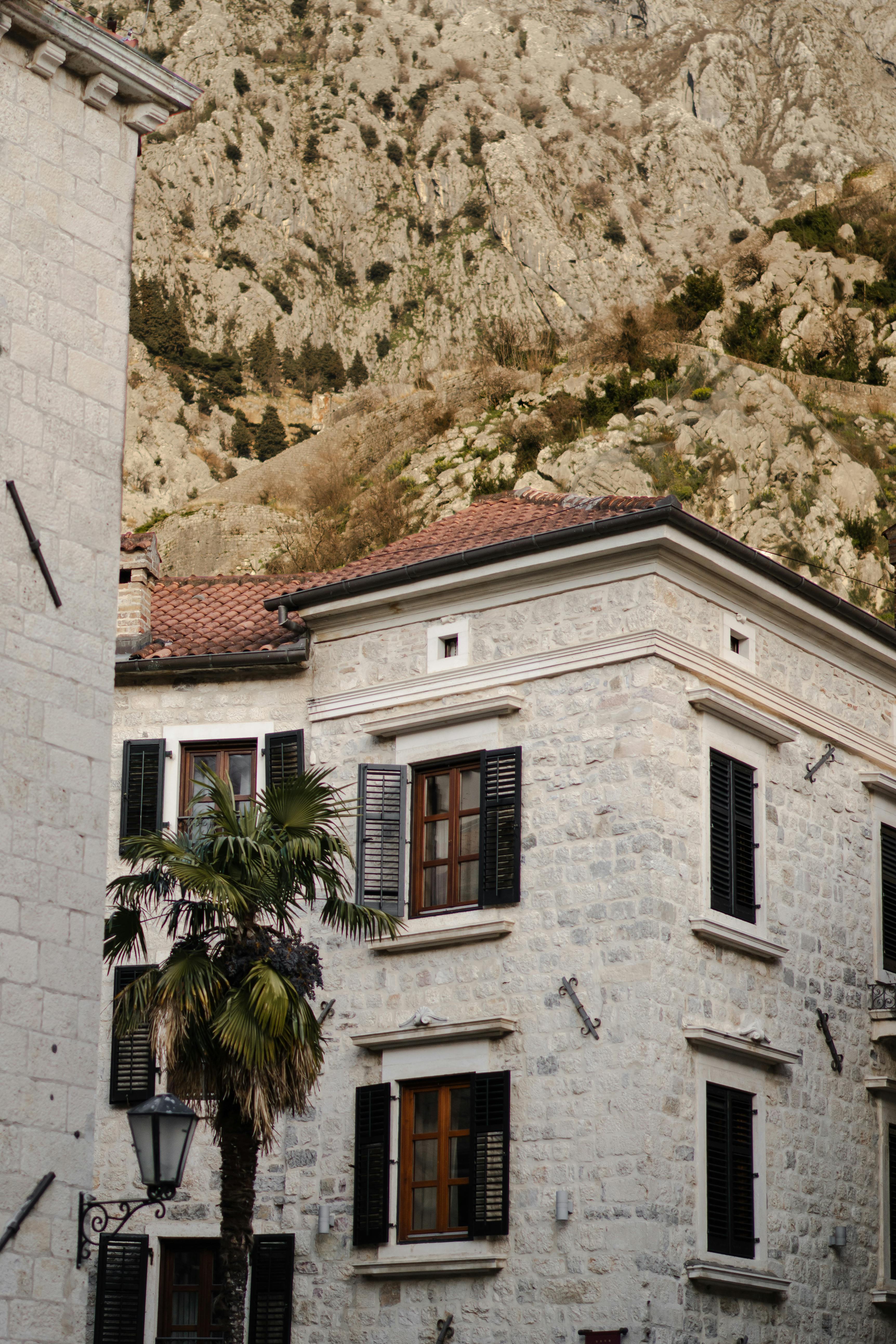 A quaint stone building with shutters in front of rocky hills, exuding Mediterranean charm.
