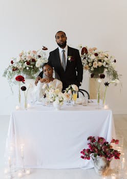 Stylish couple posed at a wedding table with beautiful floral arrangements and candles.