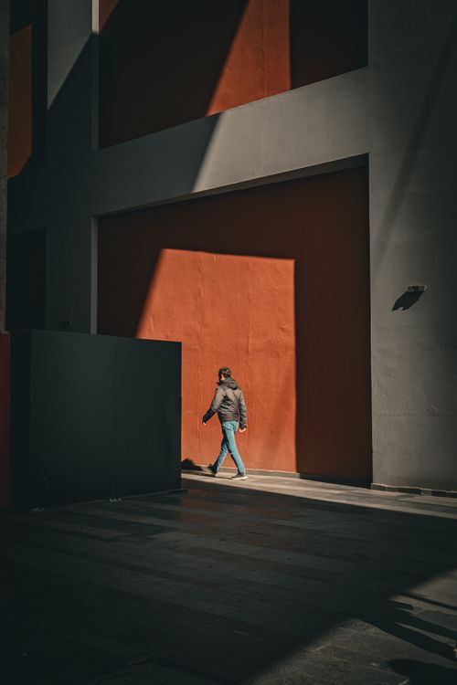 Free A solitary figure walks past a sunlit building facade in Istanbul, casting sharp shadows. Stock Photo