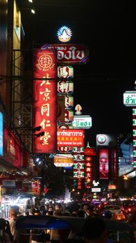 Bustling street with neon signs in Bangkok's Chinatown at night.