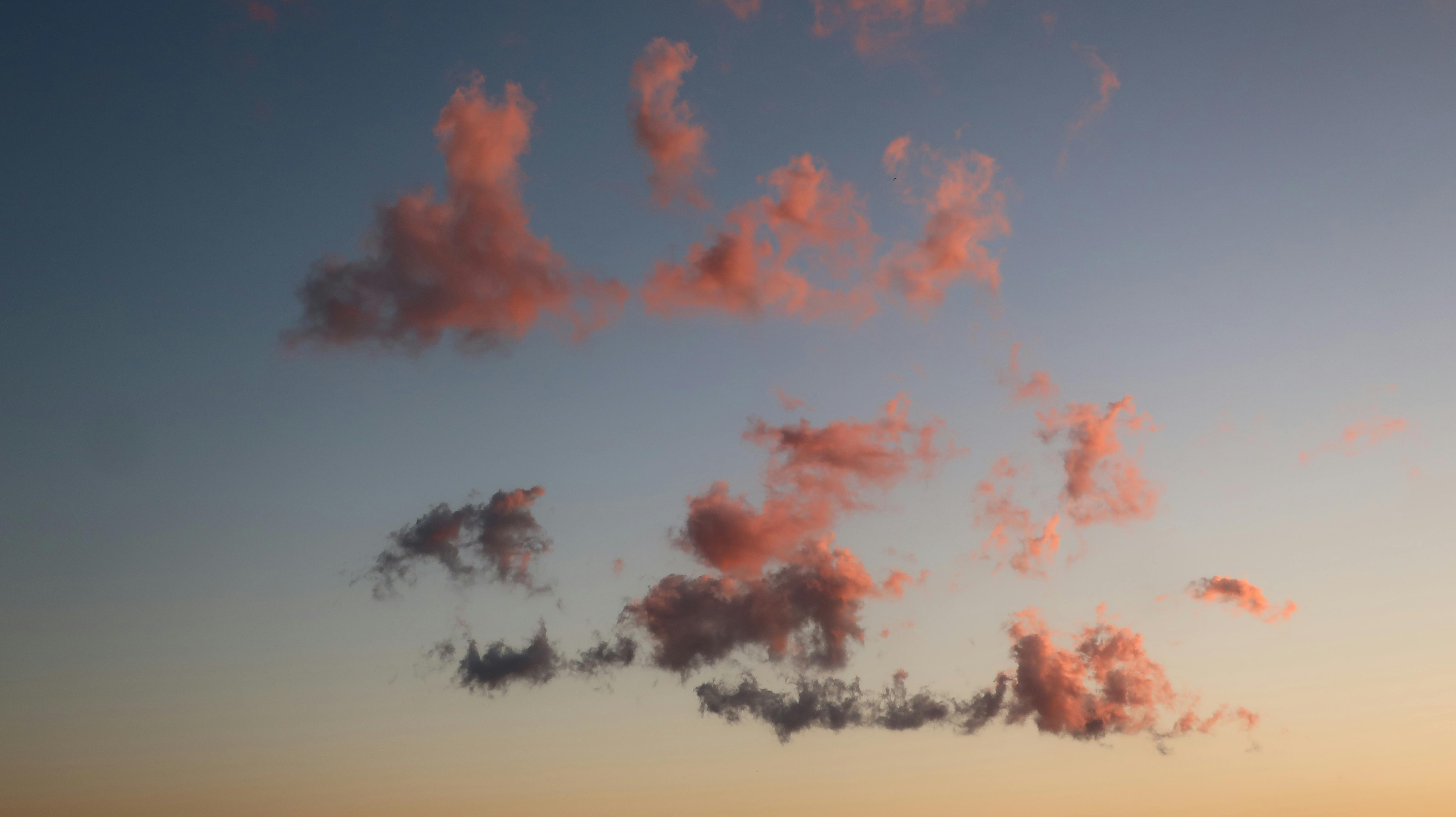 grátis Nuvens rosadas e serenas flutuam num céu azul límpido ao pôr do sol, criando uma cena tranquila. Foto profissional