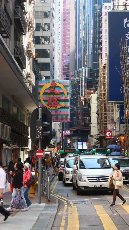 Free Vibrant Hong Kong street filled with pedestrians and traffic amidst towering skyscrapers, capturing urban life. Stock Photo