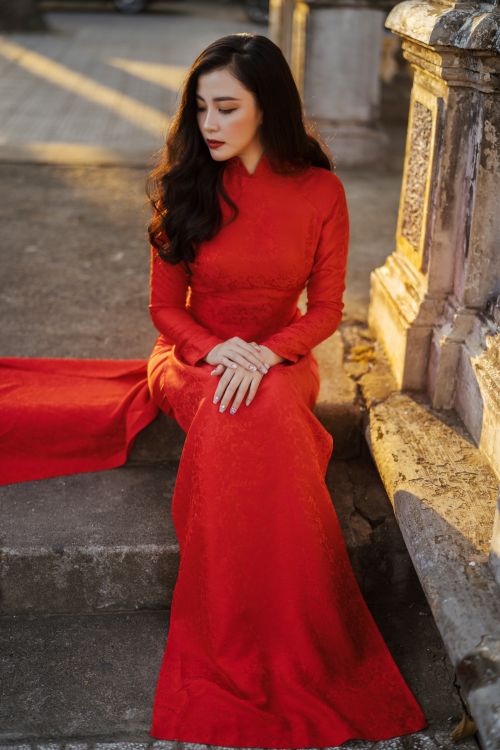 Free Portrait of a woman in a red traditional dress sitting on steps, exuding grace. Stock Photo