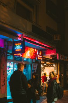 Colorful city nightlife in Frankfurt with people socializing and shopping under vibrant neon lights.