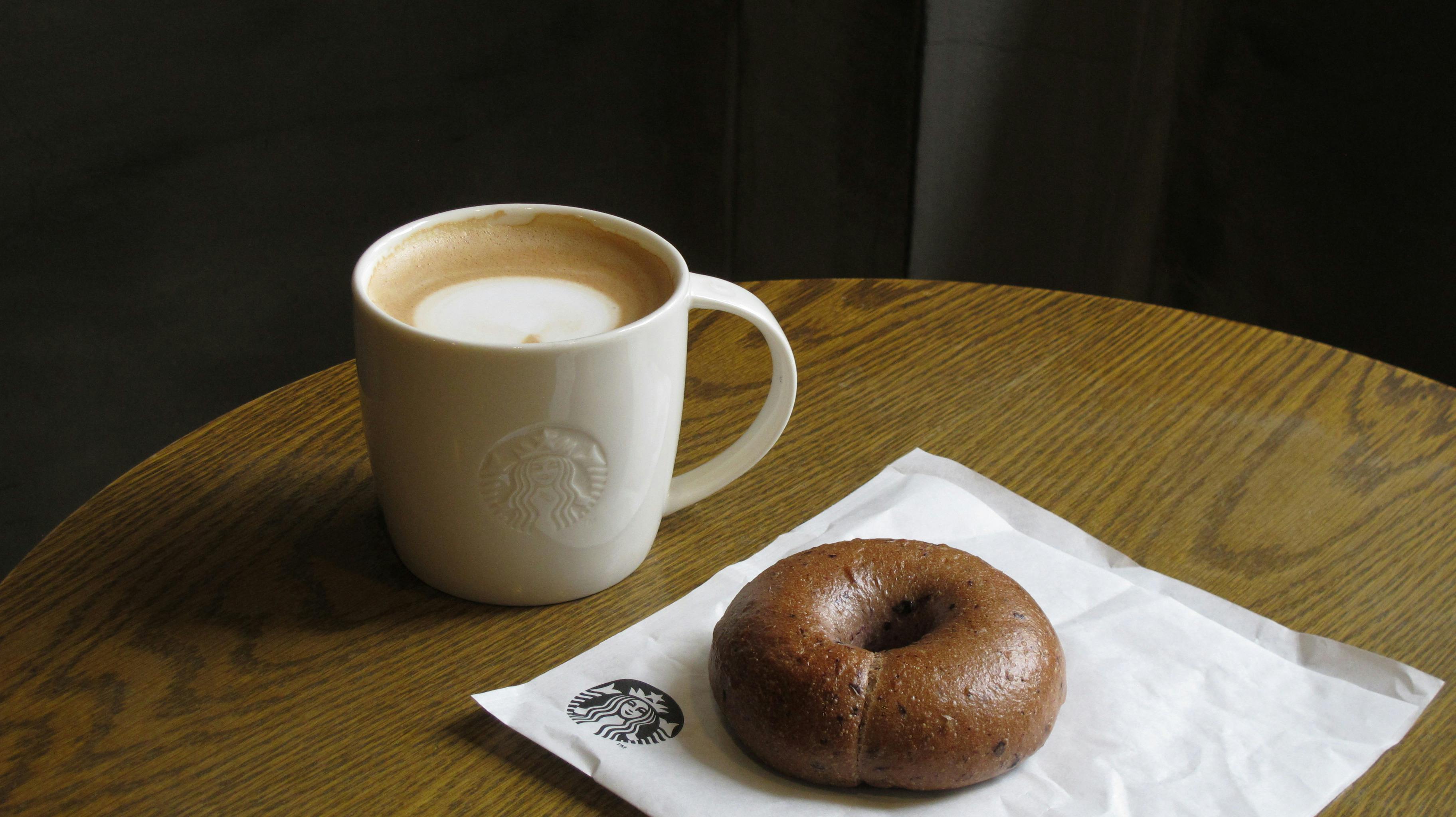 Kostenlos Genießen Sie eine entspannende Kaffeepause mit einem warmen Latte und einem Schokoladenbagel in gemütlicher Café-Atmosphäre. Stock-Foto