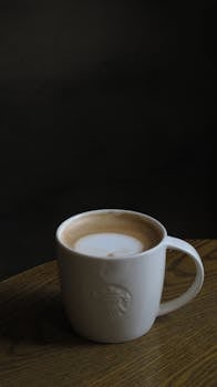 Moody shot of a cafe latte in a white ceramic mug on a wooden table, emphasizing calm elegance.