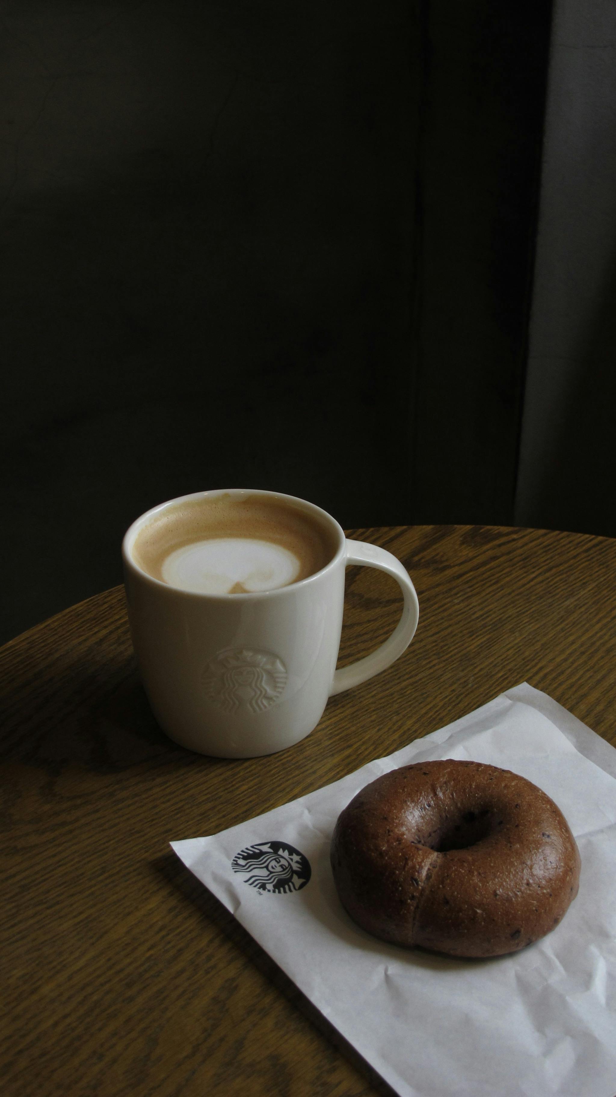 Bezpłatne Delektuj się ciepłą kawą i świeżym bajglem w kawiarni Starbucks uchwyconej w domowym zaciszu. Zdjęcie z galerii