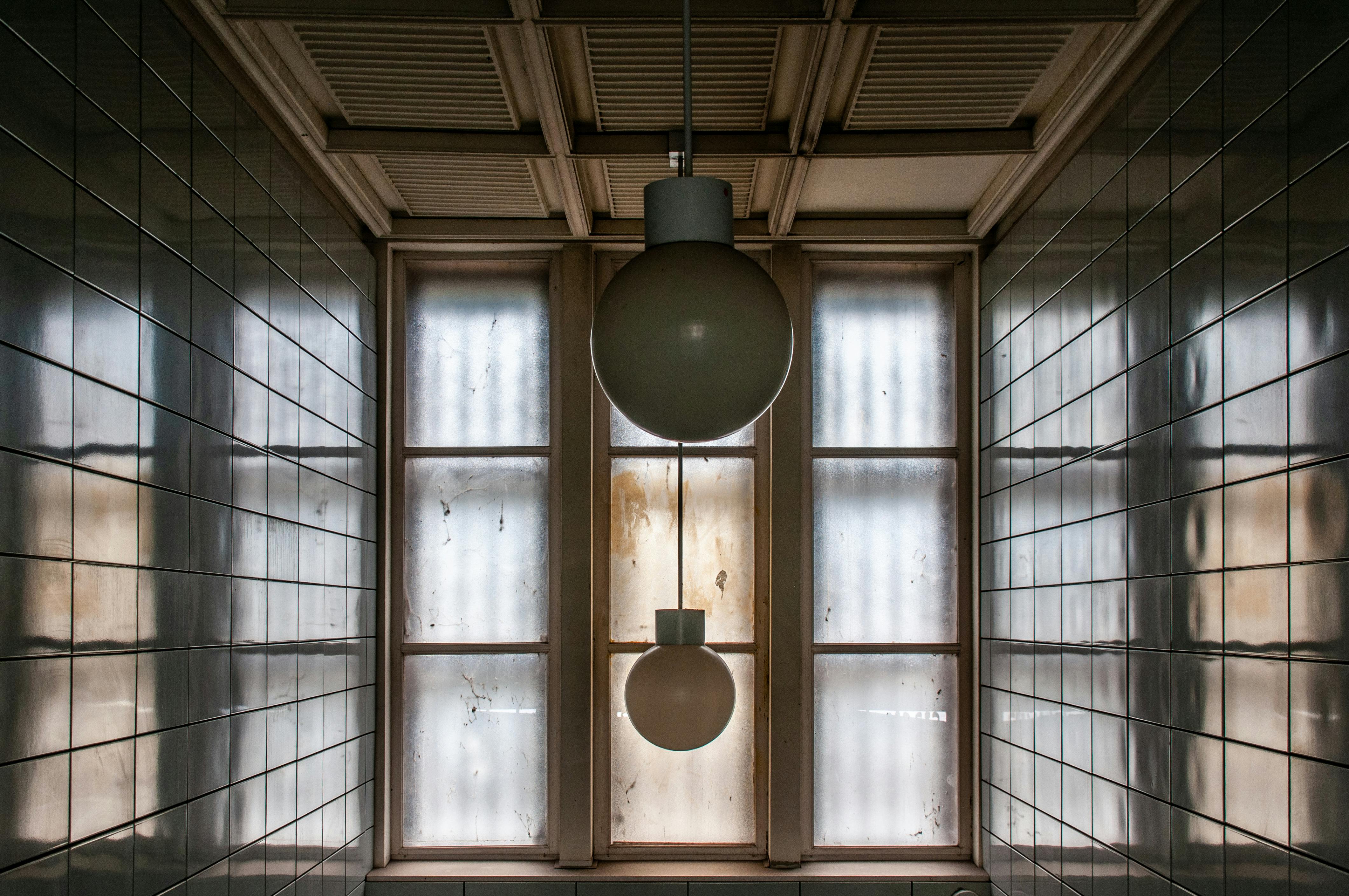 Gratis Un corridoio interno vuoto con due lampade a sospensione e pareti piastrellate d'epoca, che creano un'atmosfera retrò. Foto a disposizione